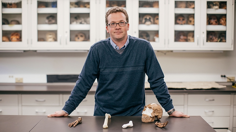 A faculty member stands with some bone fragments